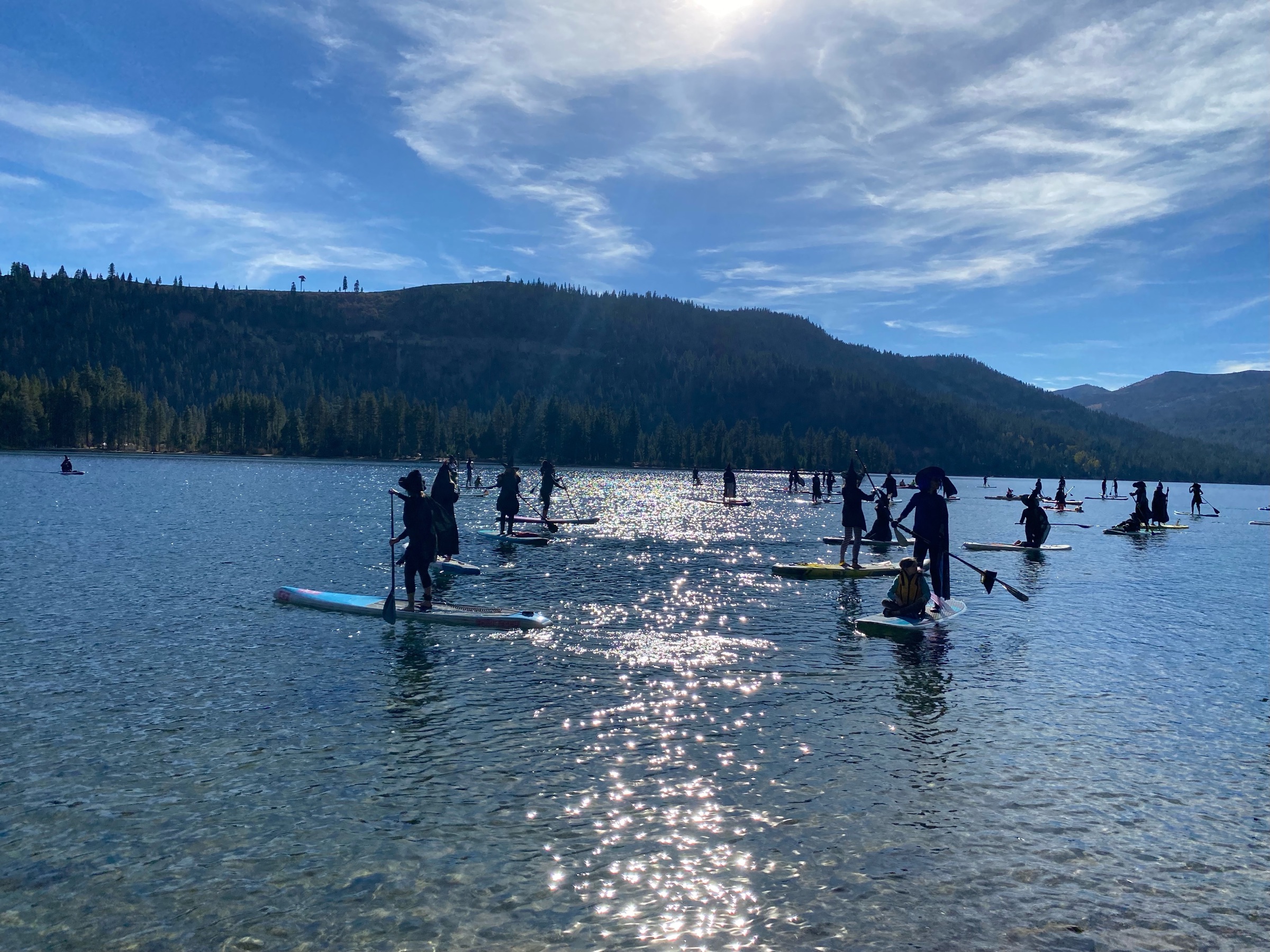 A group of costumed paddlers gathered on Donner Lake beneath a bright blue sky.