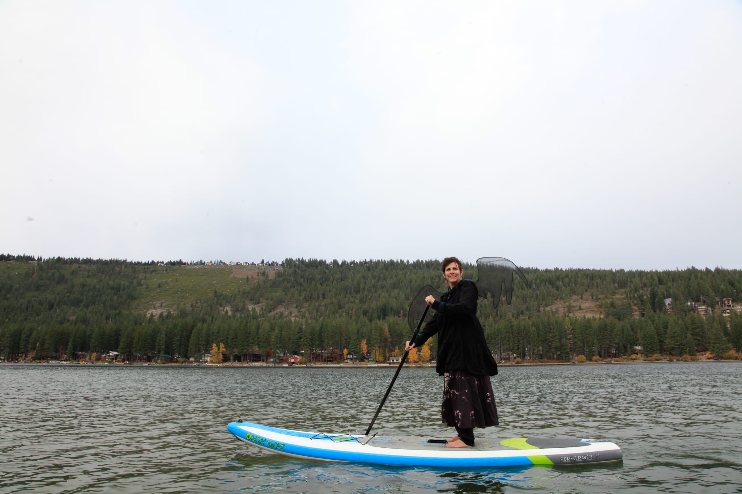 A costumed paddler with dark wings stands on a paddleboard on Donner Lake.