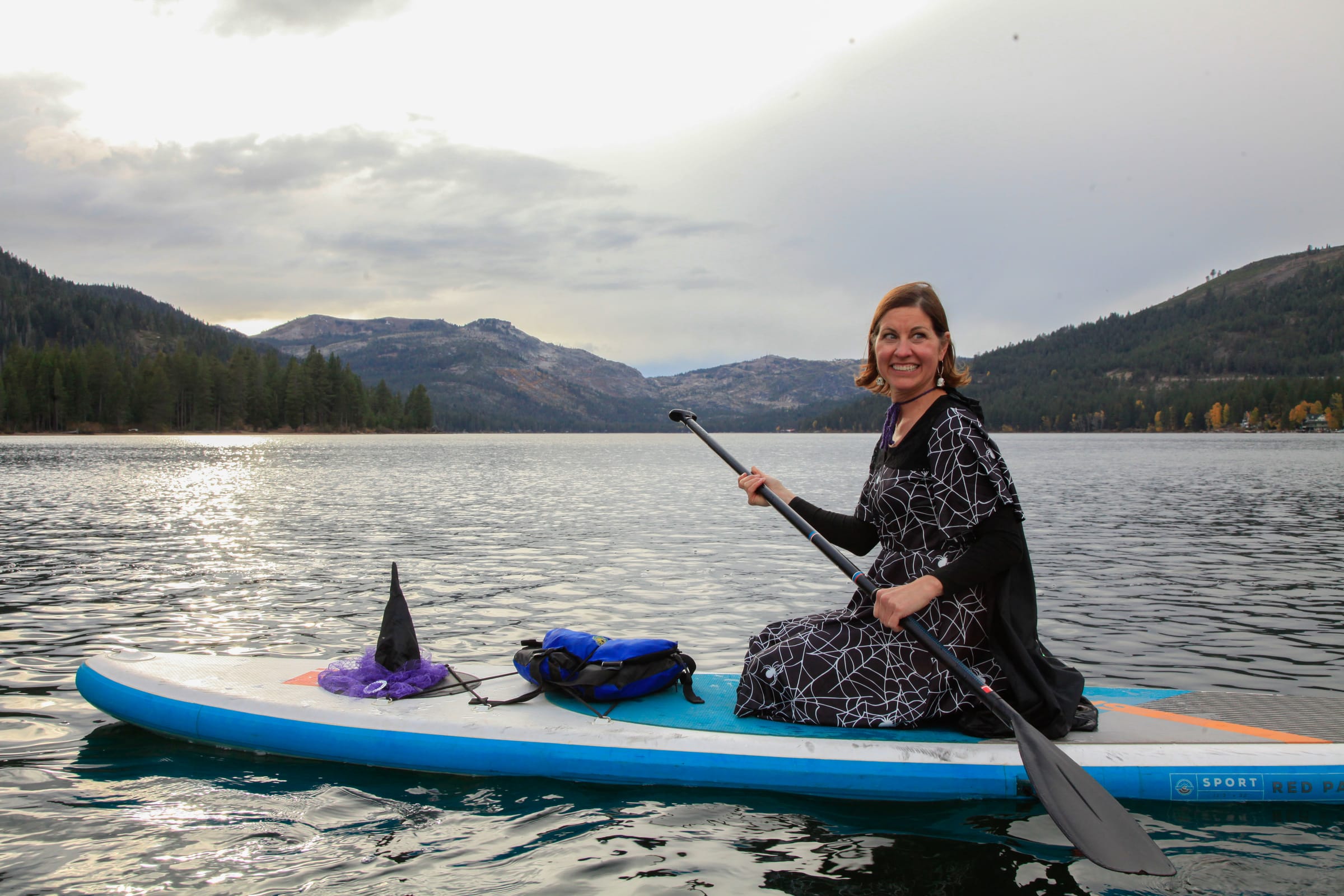 A smiling costumed paddler sits on a paddleboard beneath stormy skies on Donner Lake.